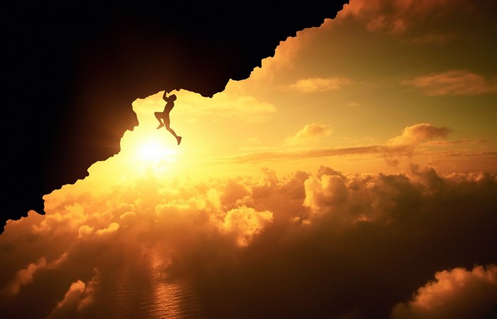 Silhouette of a climber hanging from a cliff at sunset