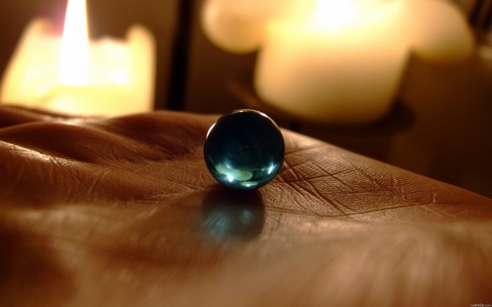 Close-up of a blue marble on a hand with candles