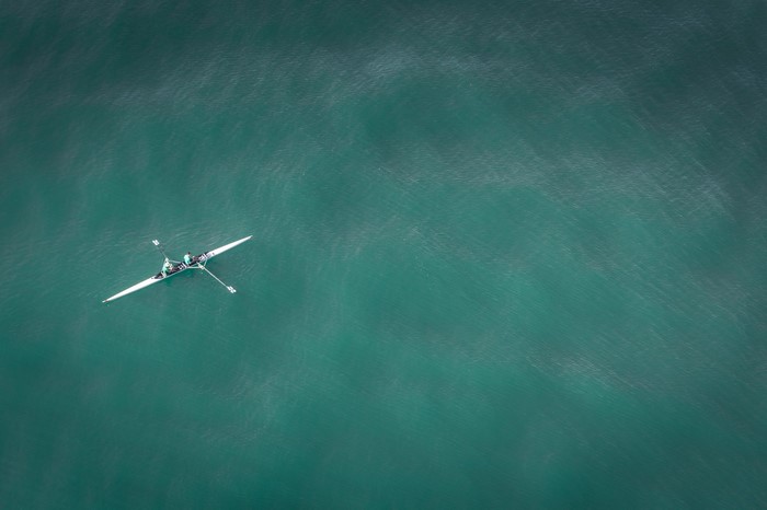 Two people rowing a white boat on a teal sea