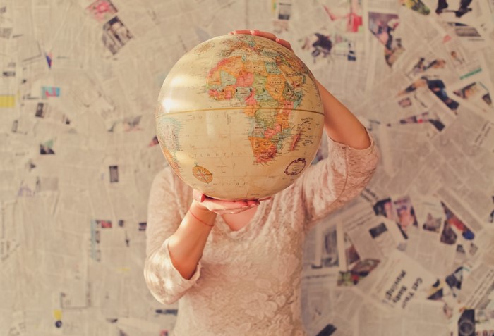 Woman holding a globe in front of newspaper wall