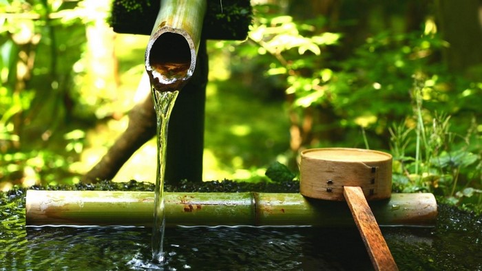 Water flowing from bamboo pipe into a basin with a wooden ladle