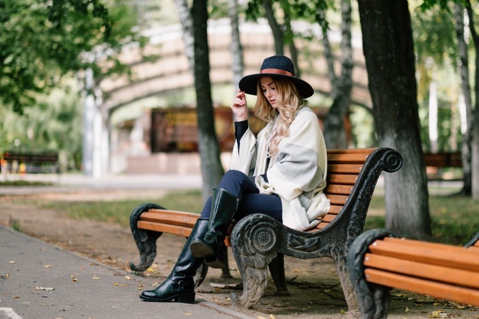 Woman in hat and boots sitting on a park bench