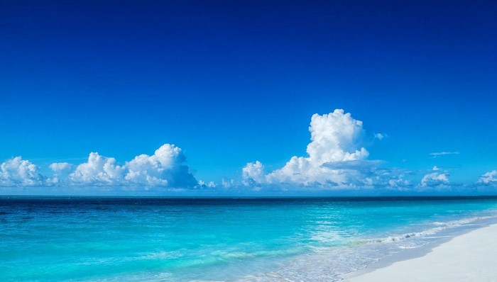 Turquoise ocean waves on a white sand beach under a blue sky with clouds