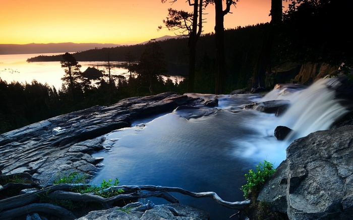 Waterfall flowing over rocks into a lake at sunset