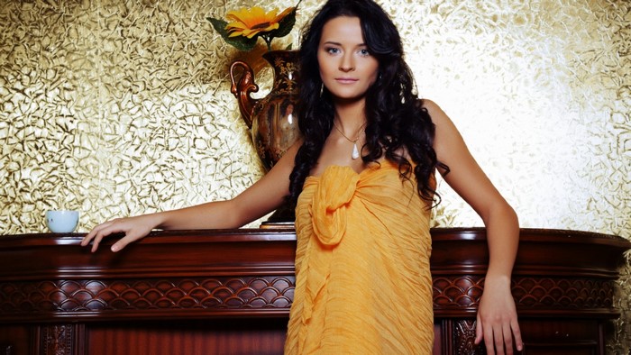 Woman in orange dress posing by fireplace