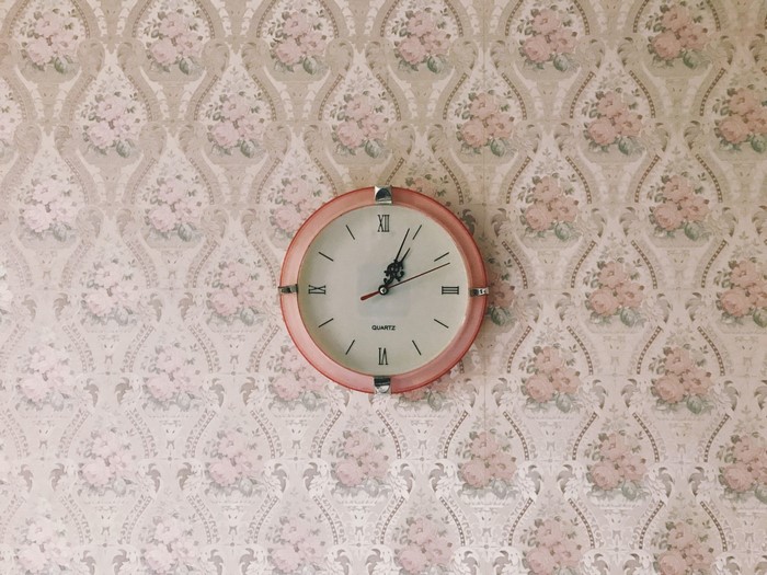 Pink analog clock on floral wallpaper