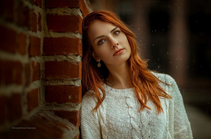 Woman with red hair leaning against brick wall