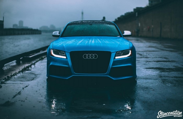 Blue Audi S5 parked on wet asphalt near a body of water