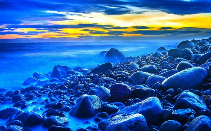 Rocky beach at sunset with blue ocean and yellow sky