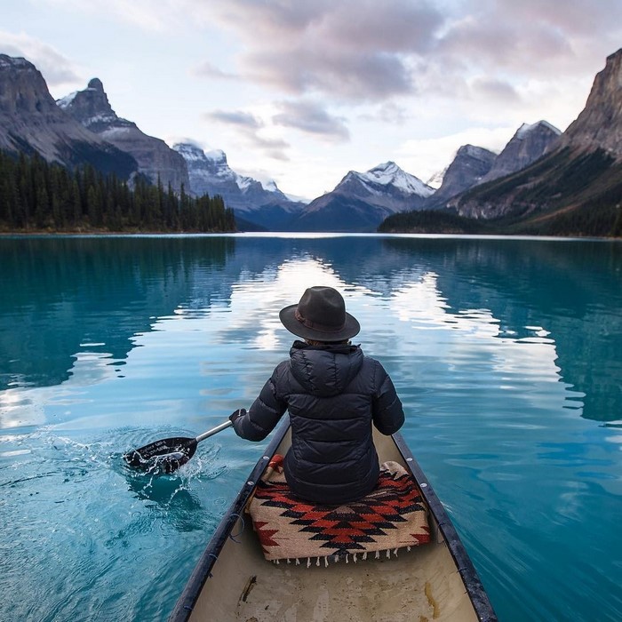 Person in canoe paddling on a turquoise lake with mountains
