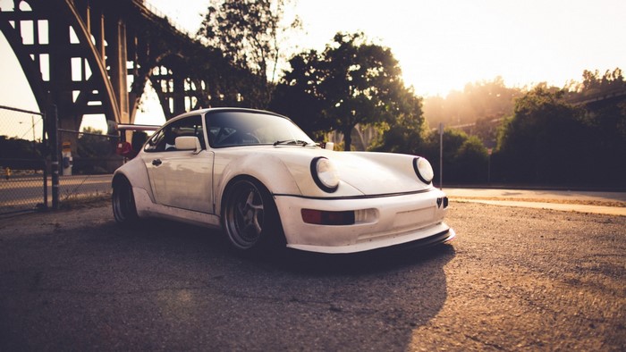 White Porsche 911 sports car at sunrise under a bridge