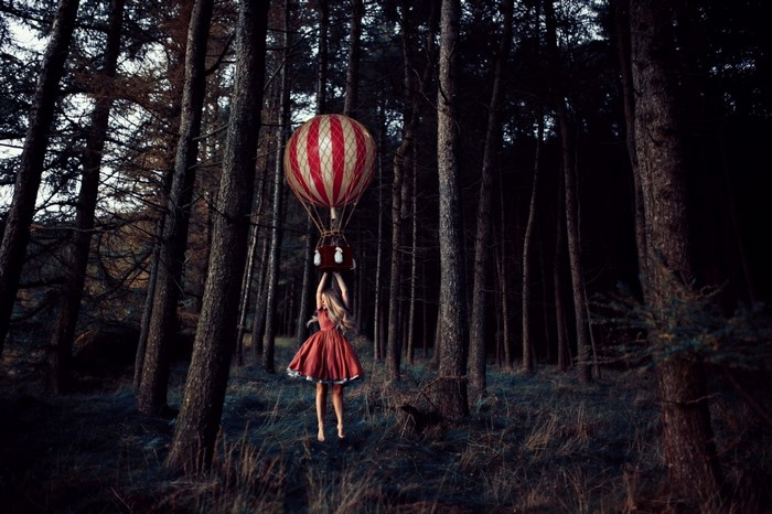 Girl in red dress holding a hot air balloon in a dark forest