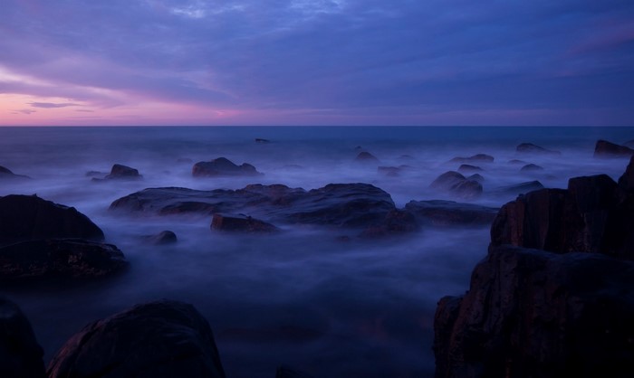 Ocean waves crashing on rocks at dusk