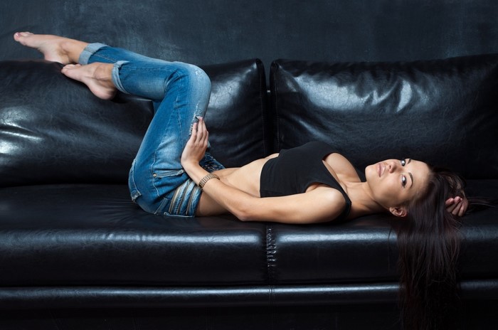 Woman in jeans lying on a black leather couch