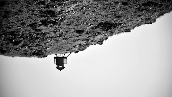 Black and white image of a rocky cliff and a small structure