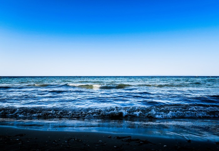 Ocean waves crashing on a dark shore under a clear blue sky