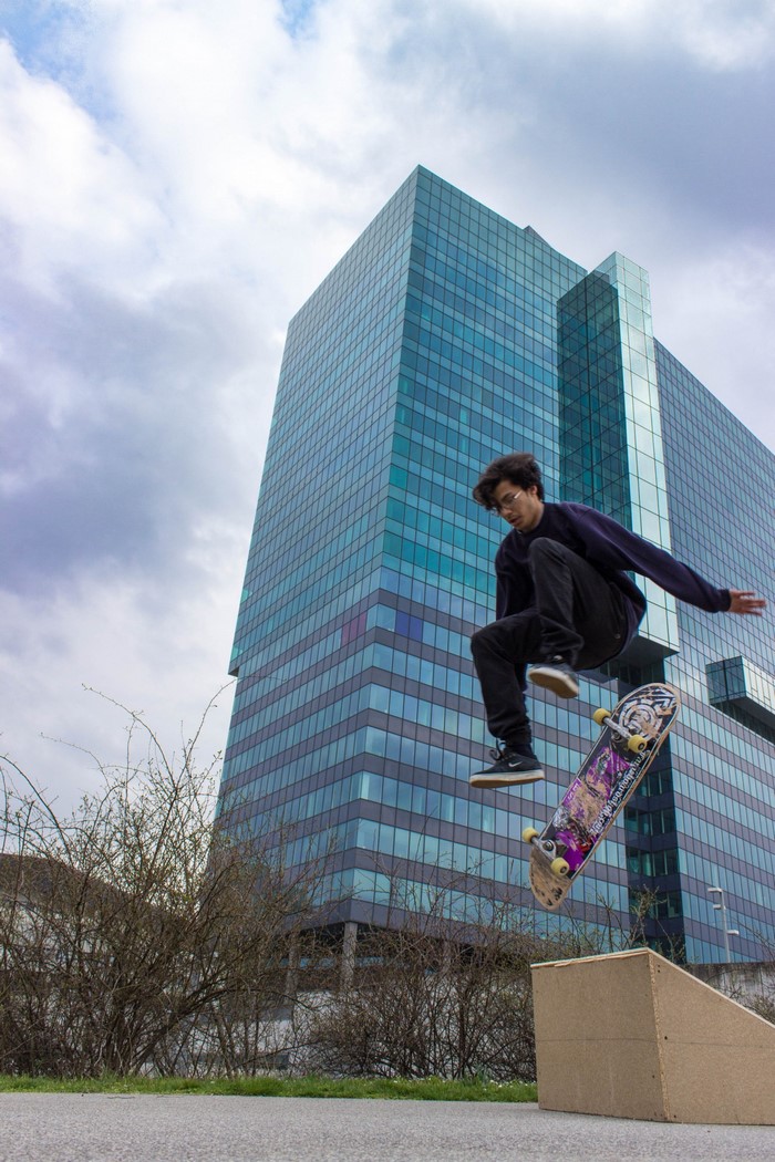 Skateboarder jumps in front of a modern glass skyscraper