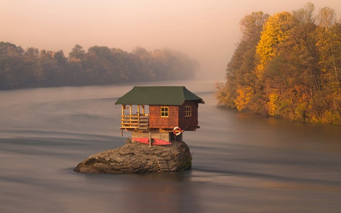 House on a rock in a river during autumn