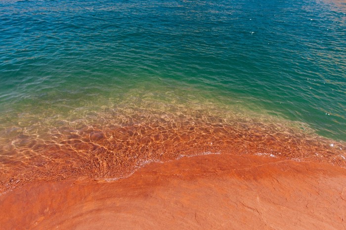 Turquoise water meets a red sandy shore