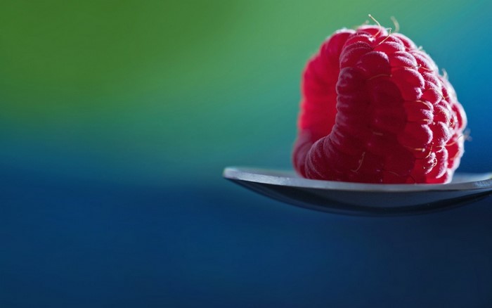 Raspberry on a spoon with a blue and green background