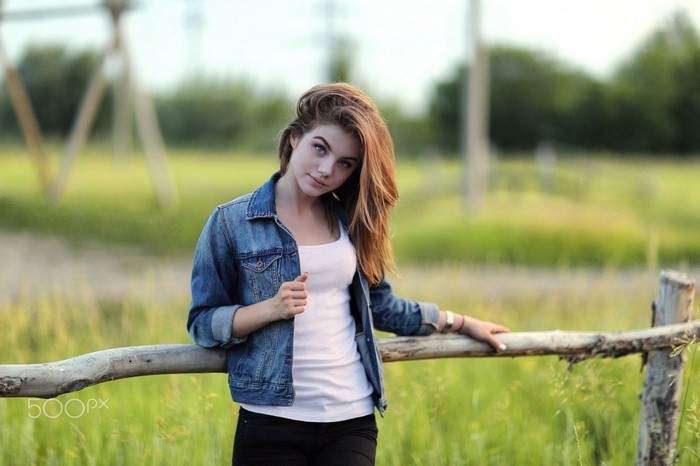 Young woman in denim jacket leaning on a wooden fence