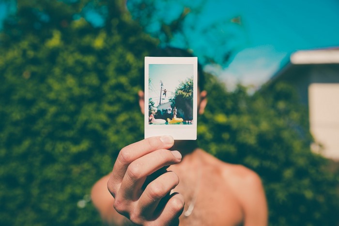 Man holding a polaroid photo of people by a pool