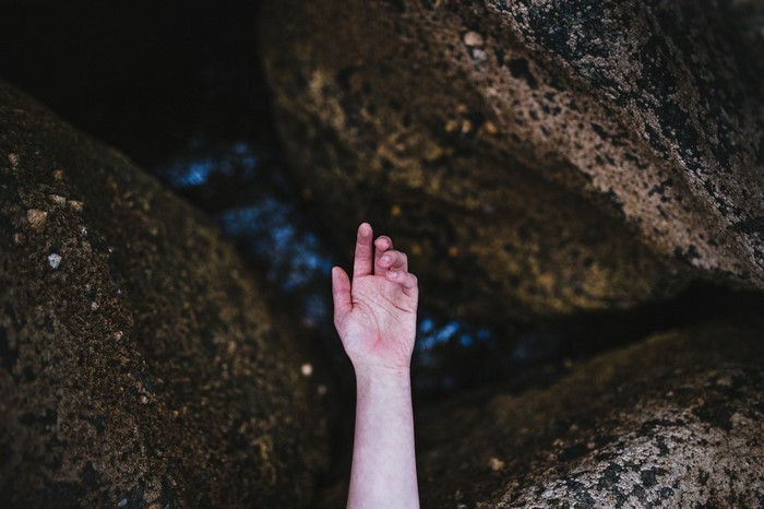 Hand reaching out from dark water between rocks