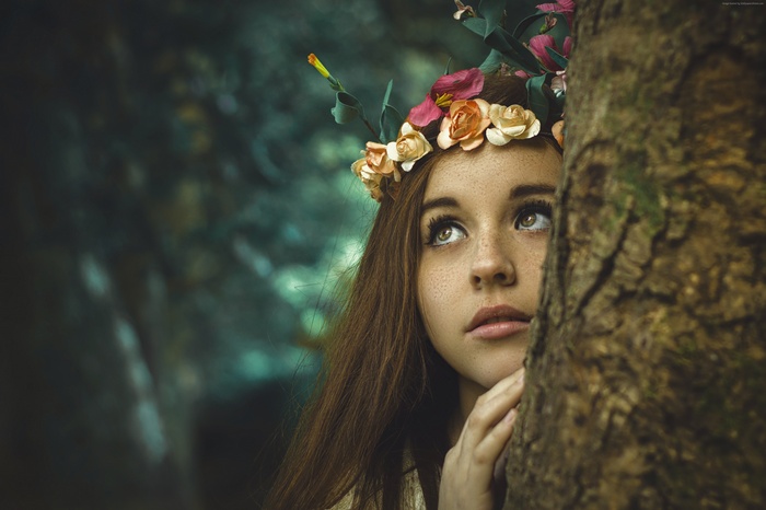 Young woman with flower crown behind a tree