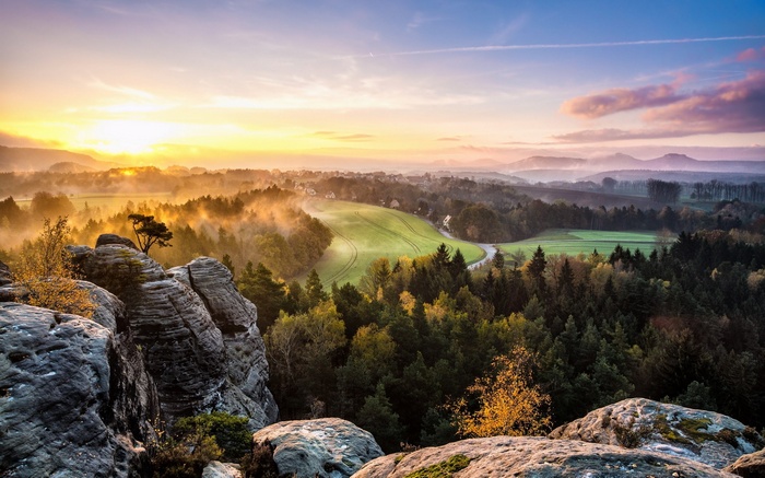 Misty sunrise over a forested valley with rock formations