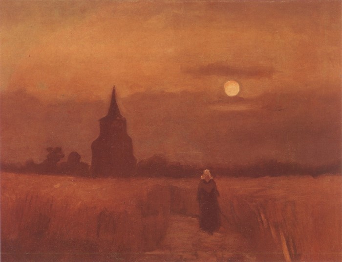 Woman walking through a field at dusk with a church tower