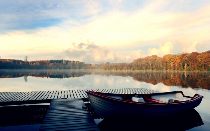 Boat docked at a wooden jetty on a calm lake during autumn