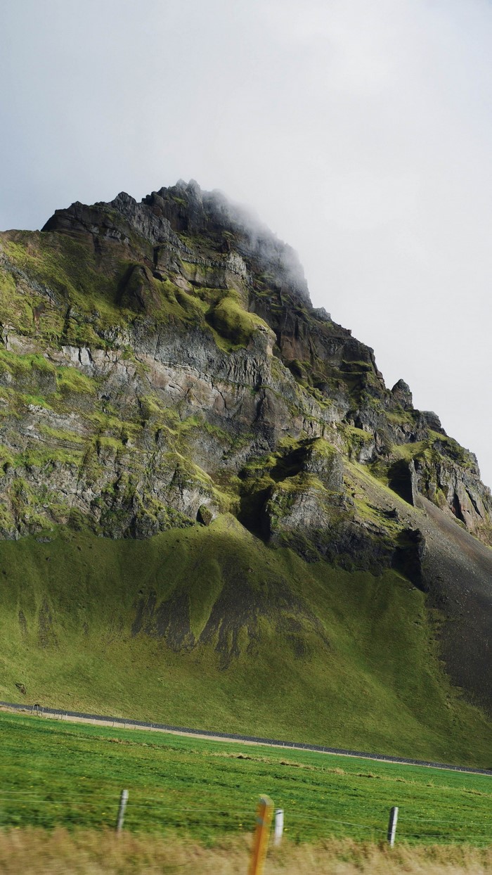 Green mountain with rocky peak and fog