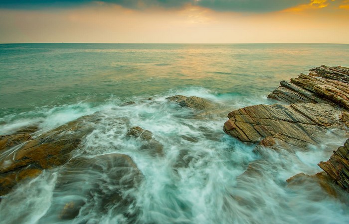 Ocean waves crashing on rocky shore at sunrise
