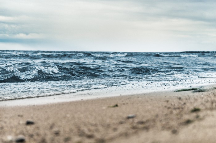 Ocean waves crashing on a sandy beach under a cloudy sky