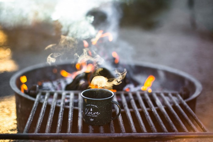 Coffee mug warming by campfire on grill