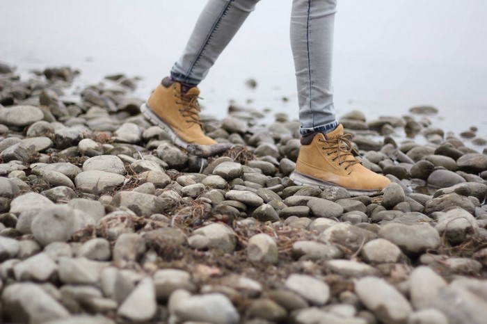 Person walking on rocks near water wearing boots