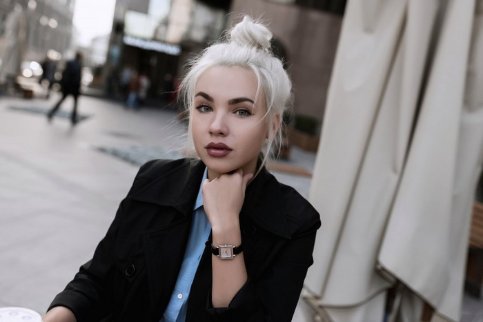 Woman with white hair wearing a black coat and blue shirt