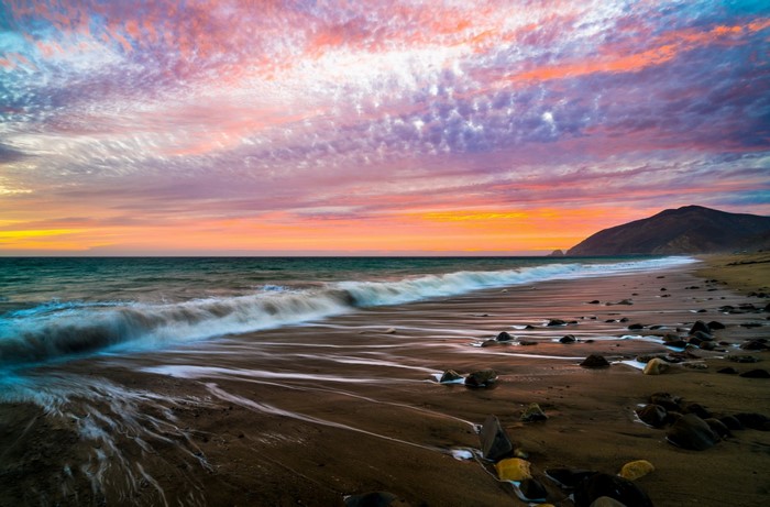 Vibrant Sunset Over Rocky Sandy Beach and Calm Ocean