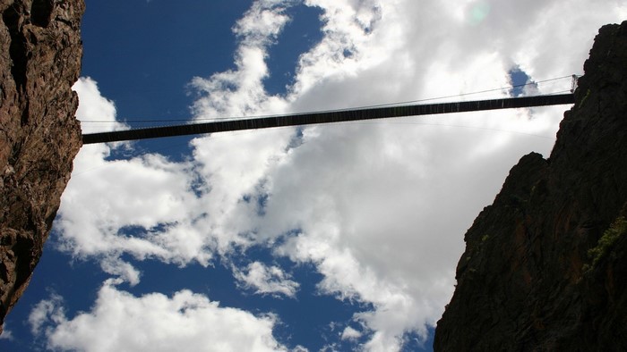 Suspension bridge between rocky cliffs under a cloudy sky