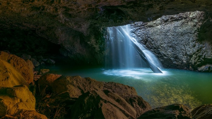 Waterfall cascading into a cave pool with rocks