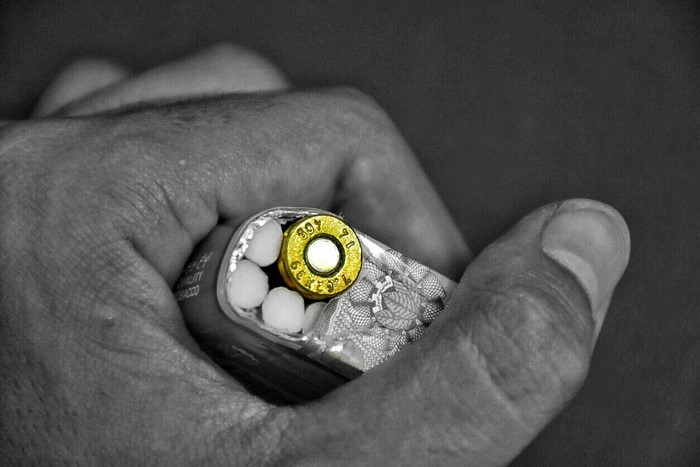 Hand holding cigarettes and a bullet cartridge
