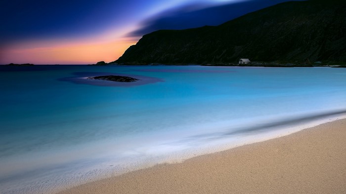 Beach at dusk with calm ocean and mountain
