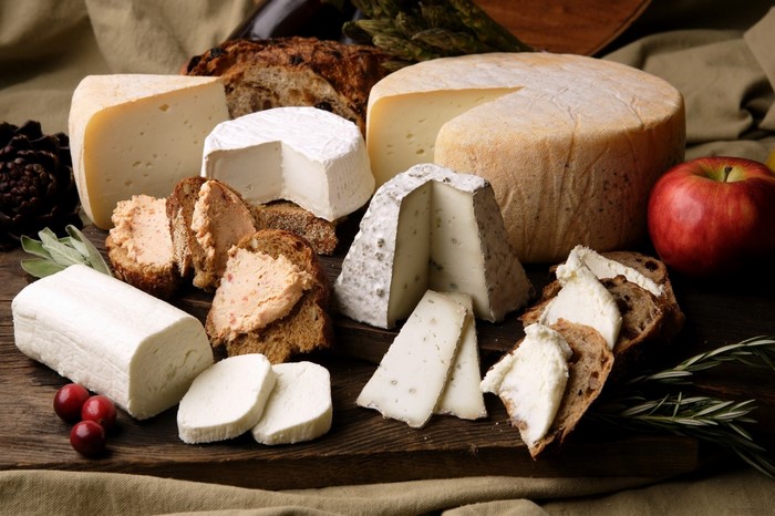Assortment of cheeses, bread, and fruit on a wooden board