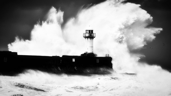 Monochrome lighthouse on a pier with large waves