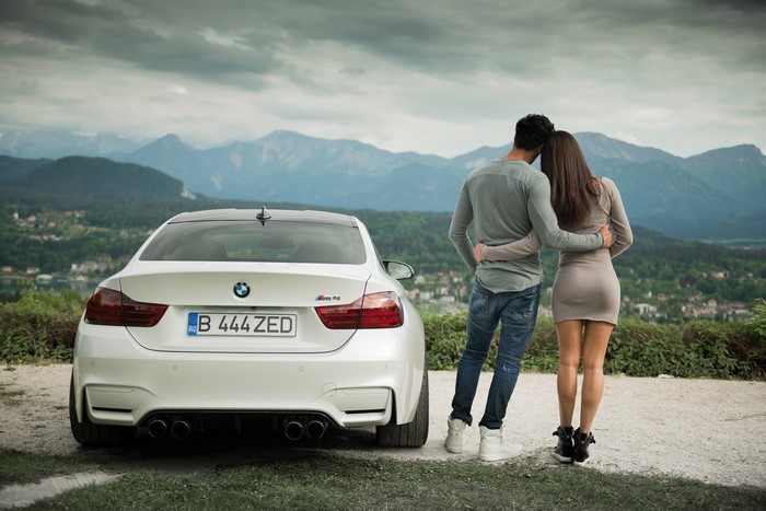 Couple embracing next to a white BMW M4 Coupe with mountains in background