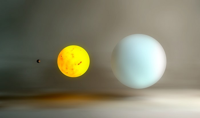 A small planet orbits a bright yellow sun next to a large blue sphere