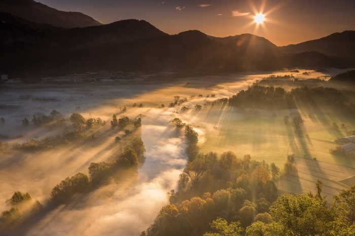 Sunlight beams through mist over a valley at sunrise