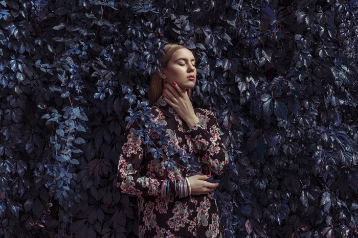 Woman in floral dress standing against dark foliage