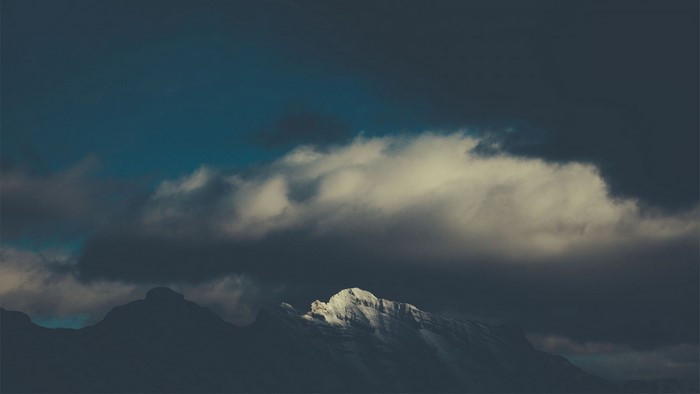 Snowy mountain peak illuminated by sunlight through clouds