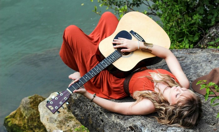 Woman in red dress playing guitar by water
